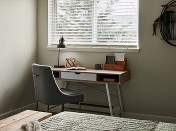 A grey chair sits in front of a desk with a lamp and some books on it.